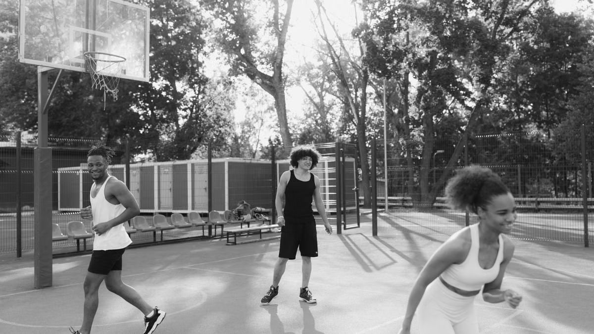 Three young adults enjoy a lively game on an outdoor basketball court.